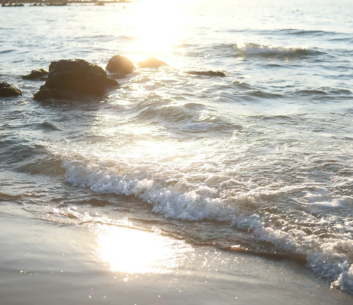 Ondas e areia iluminadas pelo sol ao entardecer; imagem editorial, não é produto da Mandala